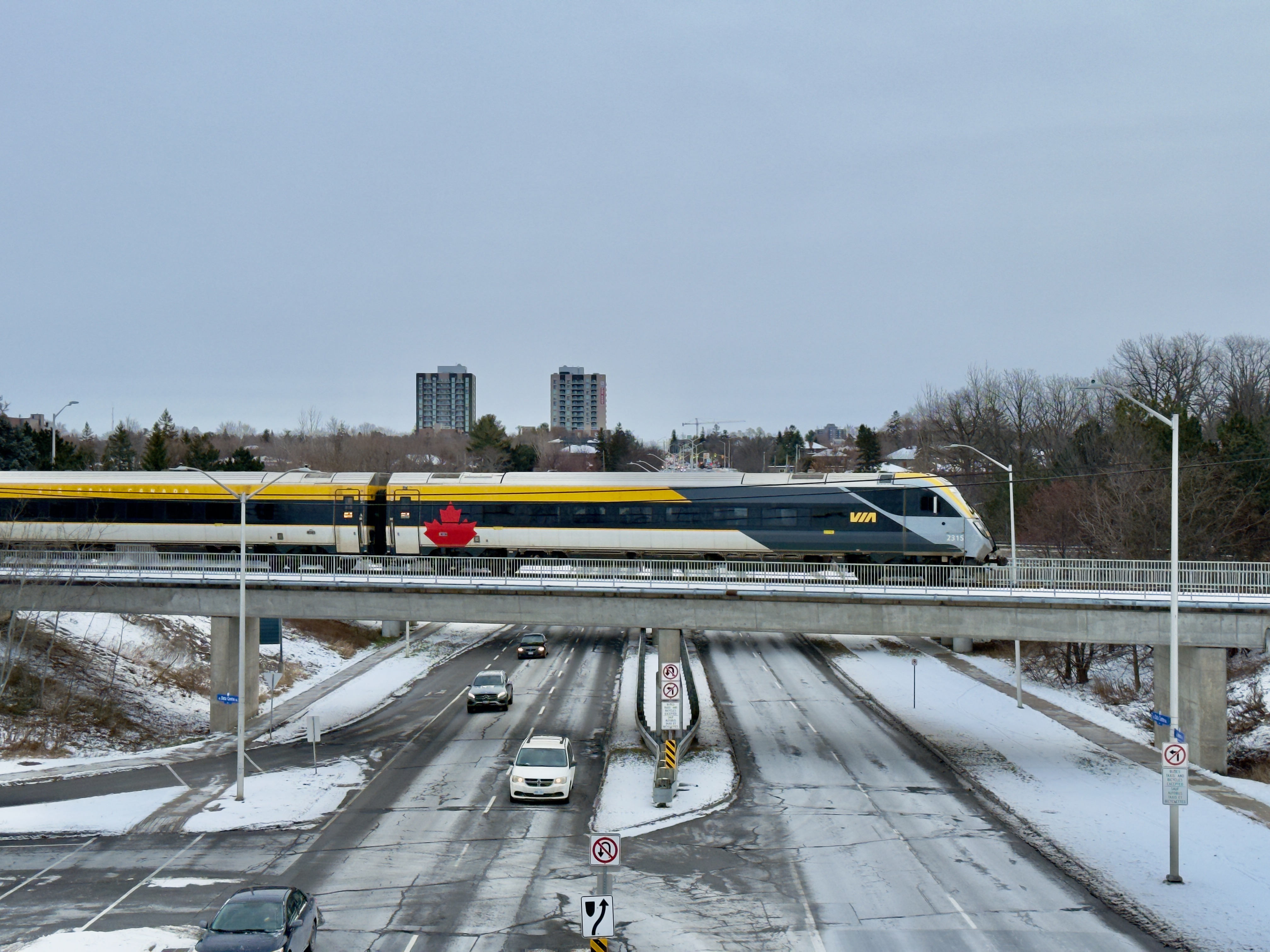 Looking down Heron road. Cars are on the road, and a bridge crossing the road has a train on it.